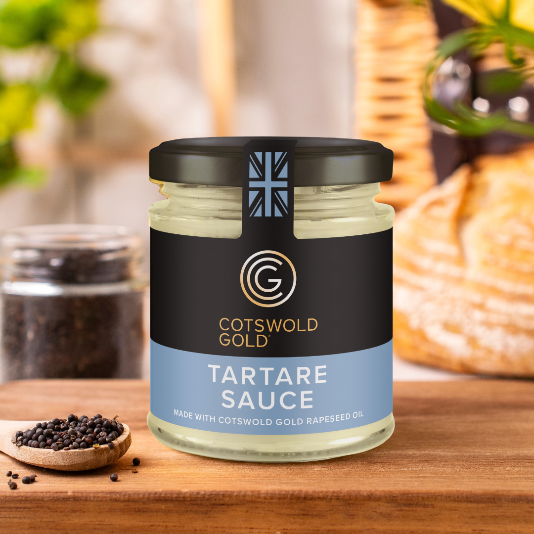 A jar of Cotswold Gold Tartare Sauce on a wooden board, with ingredients like eggs and rapeseed oil visible in the background.